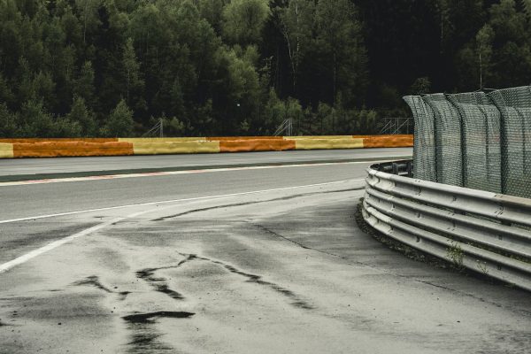 Virage de circuit bordé de vibreurs orange et de rails, entouré de forêt